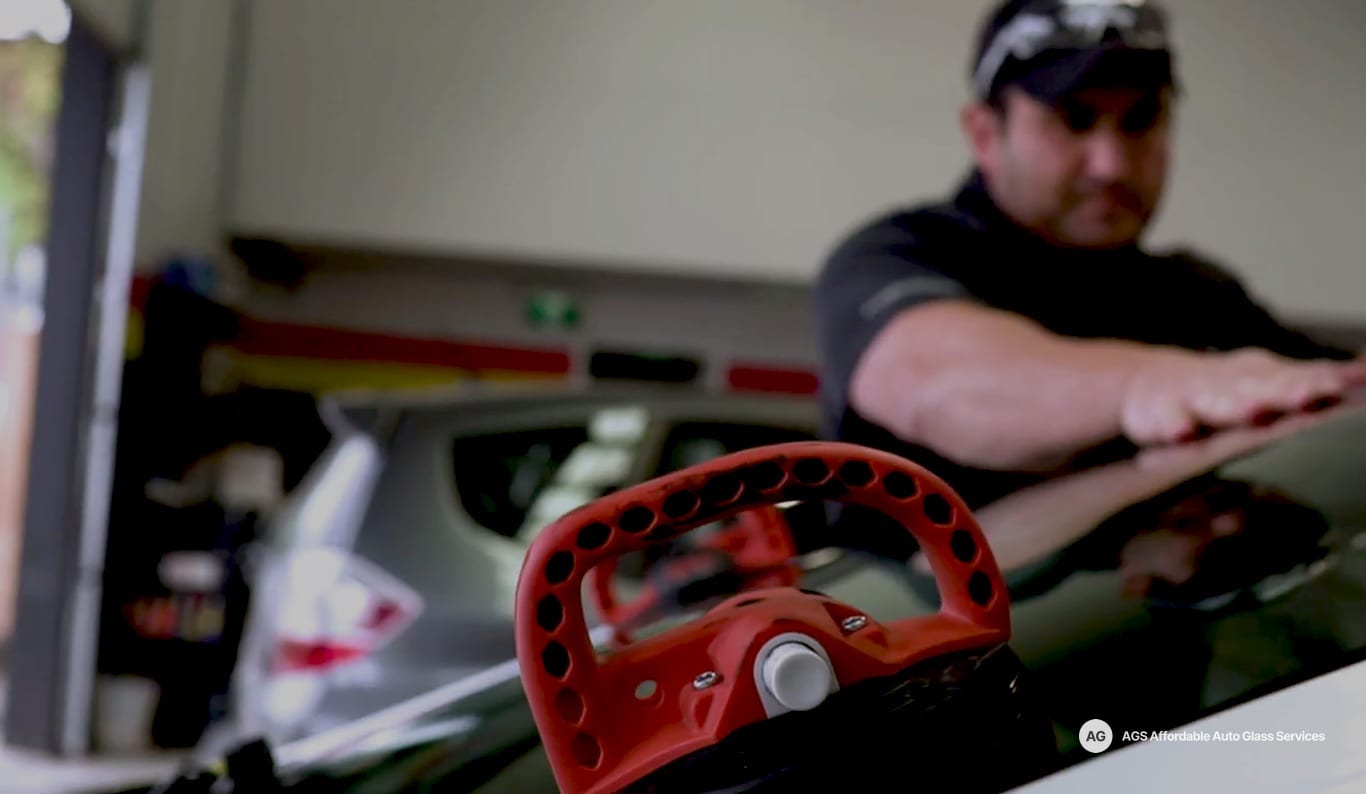 Technician setting a windshield with a red suction cup tool in a garage