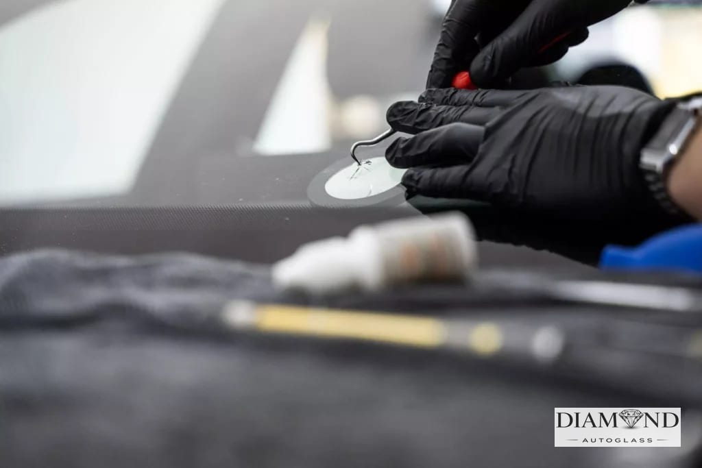 Gloved technician using a hand tool on a windshield chip repair