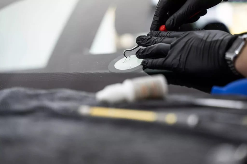 Gloved technician using a hand tool on a windshield chip repair