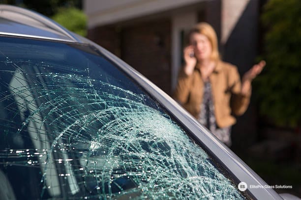 Cracked windshield on a car with a woman on the phone in the background