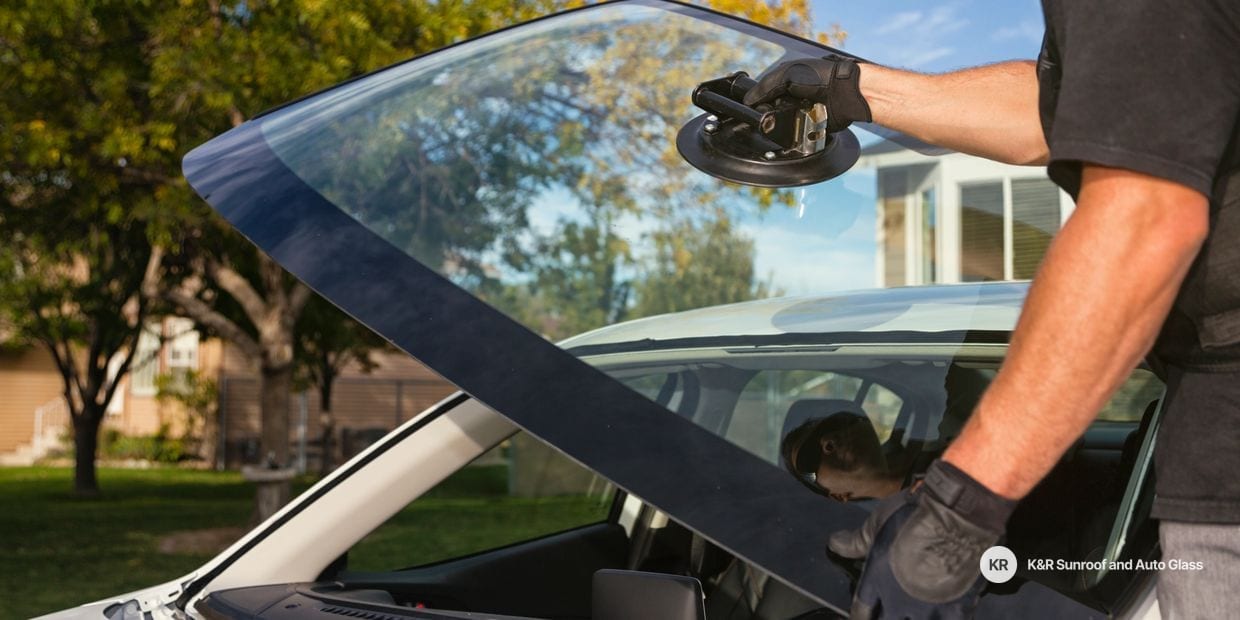 Technician using a suction cup tool to lift a windshield into place on a car