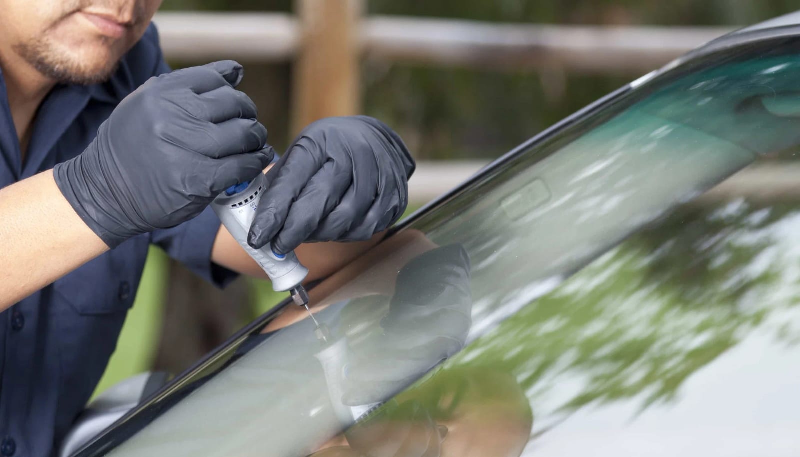Technician in gloves using a tool to repair a chip in a windshield