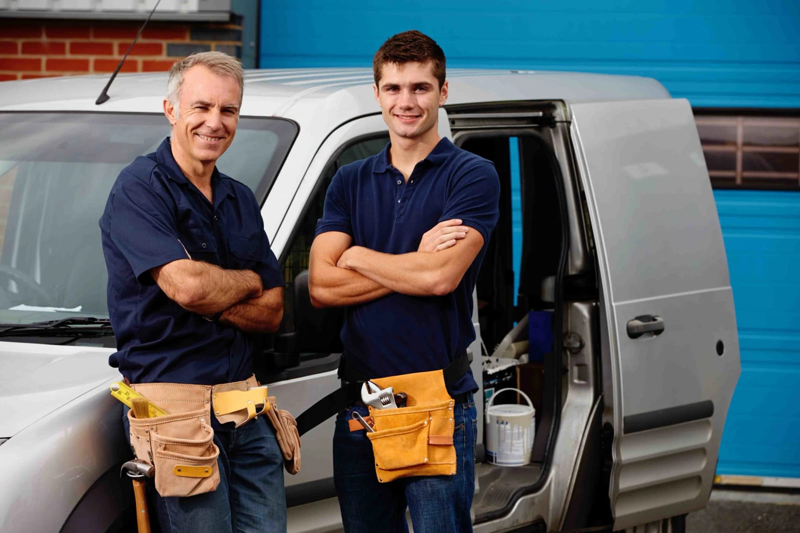 Two technicians standing with arms crossed beside a work van